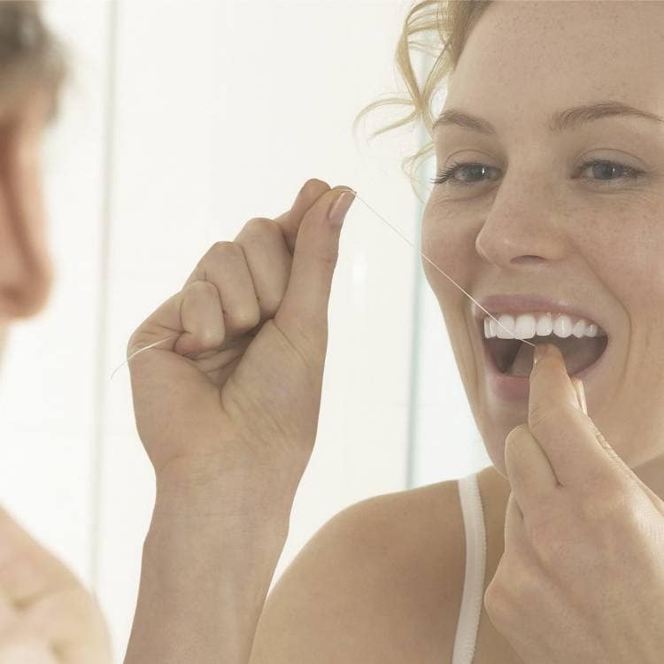 Uśmiechnięta kobieta używająca nici dentystycznej