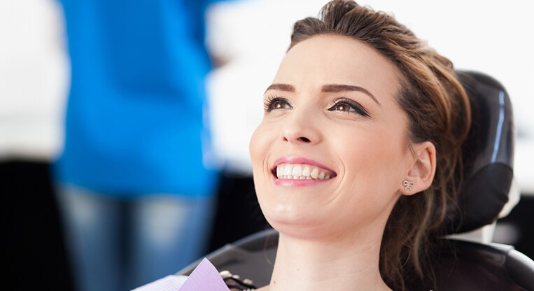 Uśmiechająca się pacjentka siedzi na fotelu dentystycznym